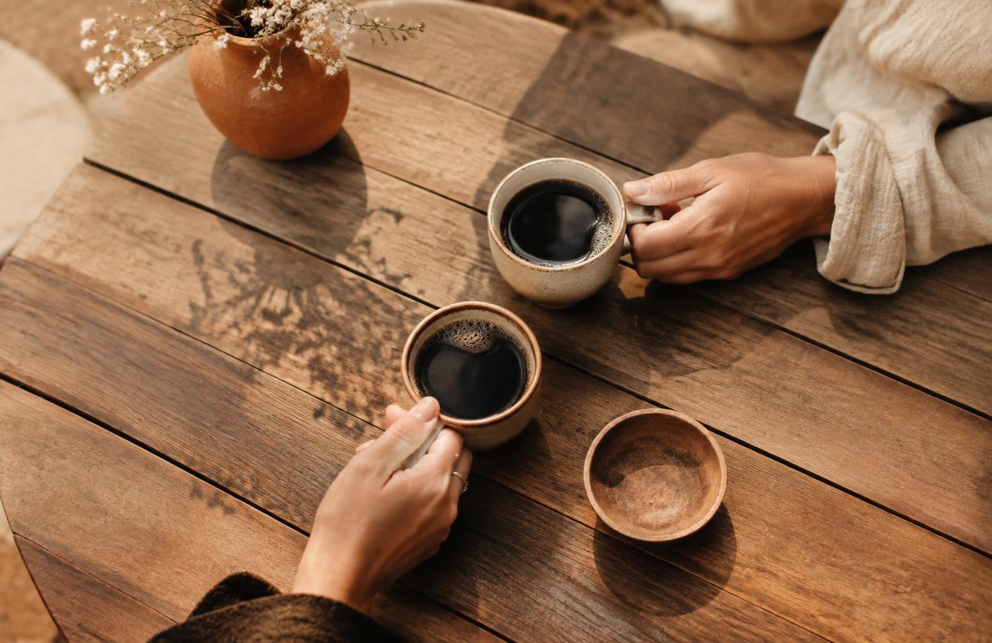 Deux mains partageant des tasses de café sur une table en bois